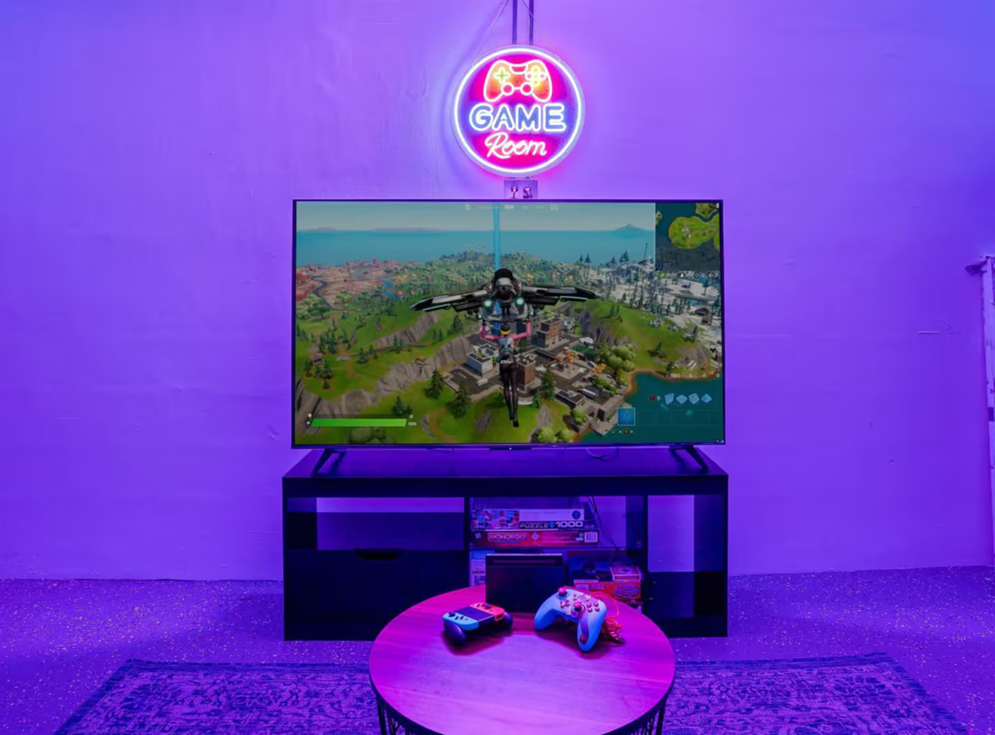 Game room with neon "GAME Room" sign, large gaming TV, controllers, and LED lighting